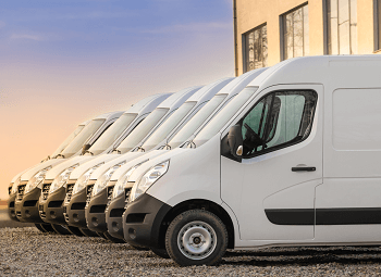 several white commercial vans parked in a row in a lot