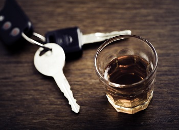 set of car keys on a table beside a glass of alcohol