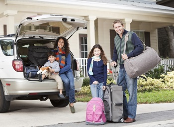 a family of four with two young children have their bags packed and ready to load into their SUV before going on a road trip